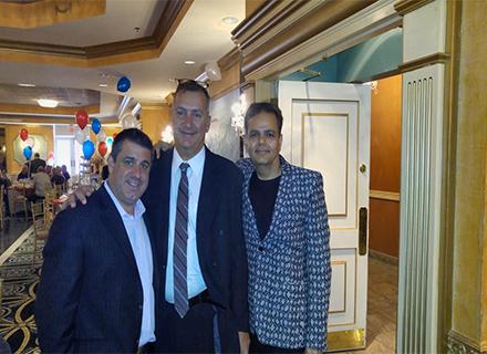 Raj in a patterned blazer with two friends at a town celebration