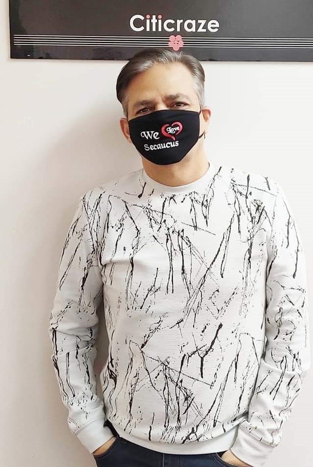 Raj wearing a 'We Love Secaucus' face mask beneath the Citicraze sign at his office